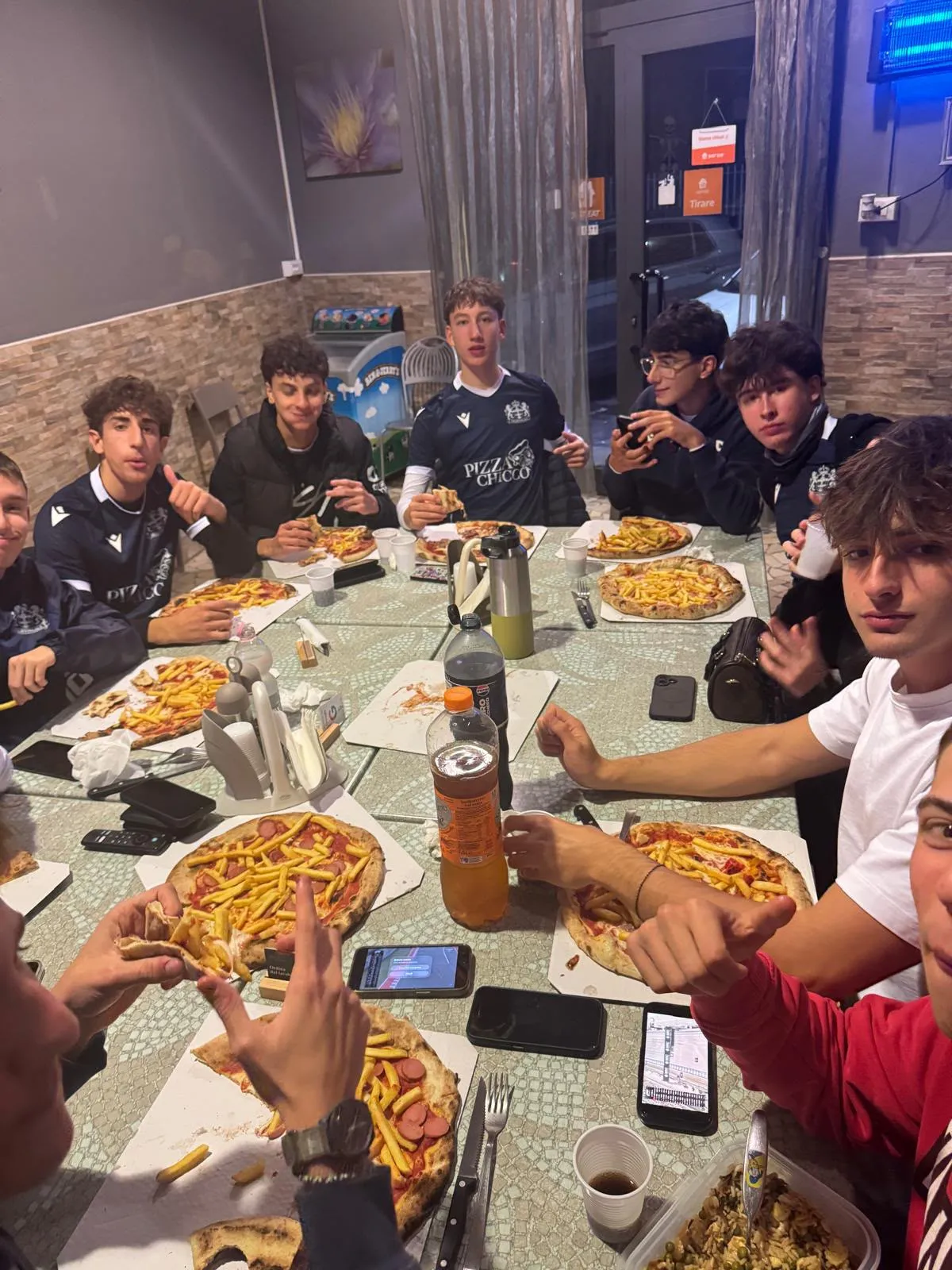 Ragazzi con la maglia Pizza Chicco a tavola nella sala, con le pizze